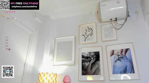 Media: Video of a minimalist, white-walled room with framed line drawings and a white air conditioner. A lamp with a yellow and white patterned shade sits on a shelf.