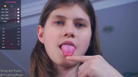 Media: Video of a young Caucasian woman with long brown hair, blue eyes, and light skin, sticking out her tongue, wearing a pink shirt. Background shows a \"Telegram Public\" interface.