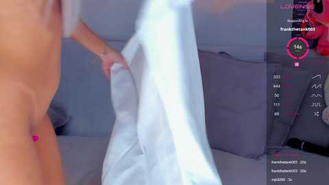 Media: A blurred video shows a topless person with fair skin, holding a white wedding dress. The background is a soft gray, and the image includes live streaming metrics.