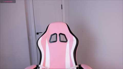 Media: Video of a pink and white ergonomic gaming chair with a curved backrest, set against a white wall and door in a minimalist room.