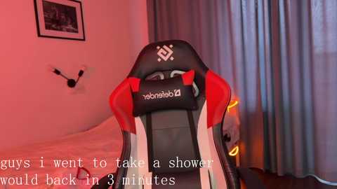 Media: Video of a black gaming chair with red accents in a bedroom with a gray curtain and a wall clock. Text overlay: \"I'll wait to take a shower in 3 minutes.\