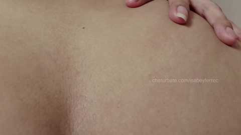 Media: A close-up video of a person's back, featuring light skin with a slight tan, showing natural body texture and pores. A hand with neatly trimmed nails rests on the shoulder.