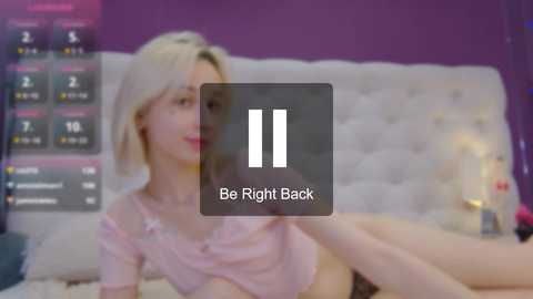 Media: Video of a young, blonde woman in a pink shirt lying on a bed with a purple wall and a digital clock displaying \"Be Right Back.\