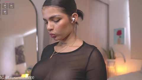 Media: Video of a woman with light brown skin and dark hair tied back, wearing a sheer black top, listening to music with white earbuds.