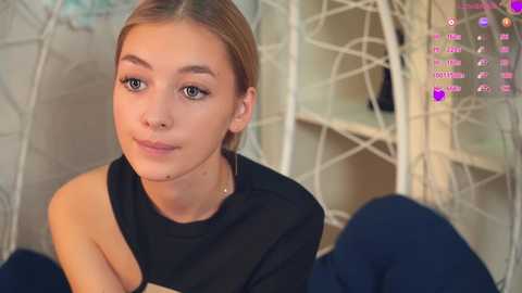 Media: Video of a young, light-skinned woman with blonde hair, wearing a black off-shoulder top, sitting indoors with a white, wireframe backdrop. Text overlays include \"Loves to play\" and \"Hates to play.\