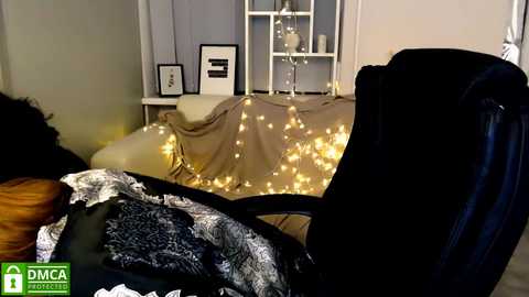 Media: Video of a cozy, dimly lit room with a beige blanket, white shelves, a black chair, and fairy lights, featuring a DMI logo.