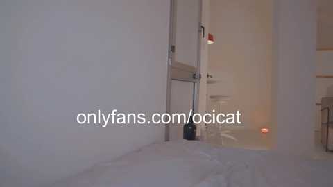 Media: A video of a dimly lit, sparsely furnished room with white walls, a black vacuum cleaner, and a small white chair. Text overlay reads \"onlyfans.com/ocicat.\