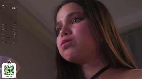 Media: Video of a young woman with long dark hair, fair skin, and a slightly pensive expression, possibly in a bathroom with a mirror and window.