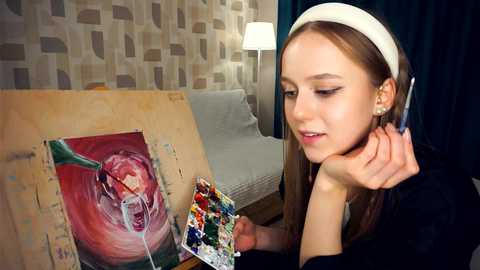 Media: Video of a young woman with straight, light brown hair, wearing a white headband and a black top, painting a vibrant, abstract painting on an easel. Background features a patterned wall and a lamp.