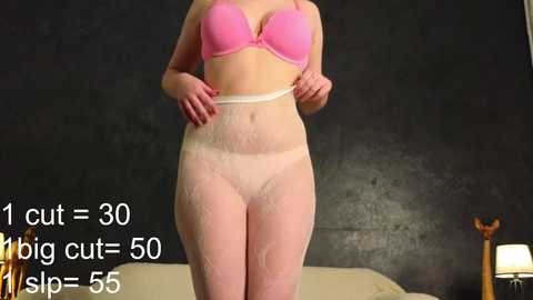 Media: Video of a fair-skinned woman in a pink bra and white sheer tights standing in a dimly lit room with a dark gray wall. Text overlay reads, \"1 cut = 30 slp-50\