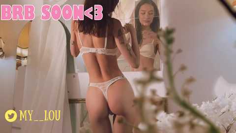 Media: A video shows a woman with long brown hair in white lace lingerie, adjusting her bra in a bedroom mirror. Text reads \"BGB SOK,\" \"MY LOU.\