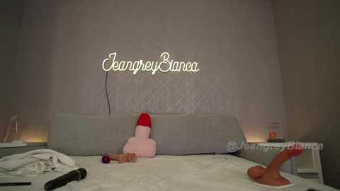 Media: Video of a woman in a bedroom with a grey headboard and white bedding. She wears a red Santa hat, a pink plush toy, and holds a dildo.