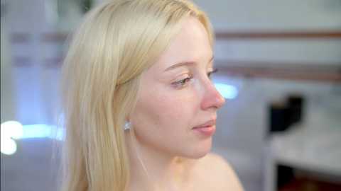 Media: Video of a fair-skinned, blonde woman with straight hair, wearing a pearl earring, in a soft-focus, modern kitchen setting.