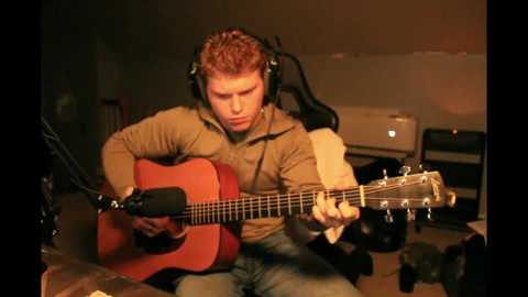 Media: A video of a man with short red hair, wearing headphones and a brown jacket, playing a red acoustic guitar in a dimly-lit studio with recording equipment and an amplifier in the background.