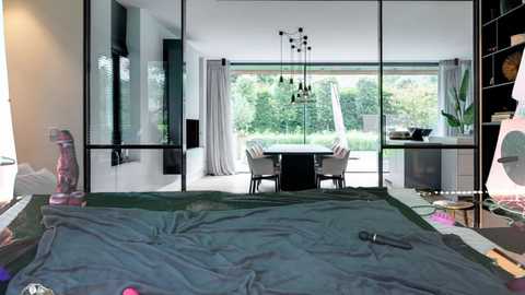 Media: Video of a modern, minimalist bedroom with a large bed covered in dark blue sheets, facing a spacious living area with glass walls, revealing lush greenery outside.