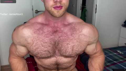 Media: Video of a muscular, shirtless man with a light beard, wearing pink lipstick, with visible chest hair, in a bedroom setting.