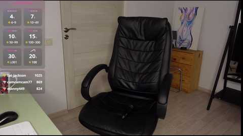 Media: A video of a black leather office chair in a minimalist room with light wooden floors, a white door, and a colorful painting on the wall.