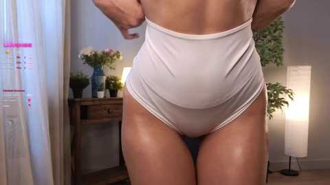 Media: Video of a light-skinned woman adjusting her white high-waisted panties, revealing toned thighs and buttocks. Background features a wooden desk with flowers, a lamp, and a tall white floor lamp.