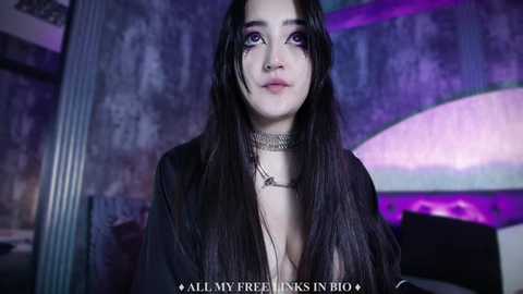 Media: Video of a young woman with long, dark hair, wearing a black choker and a low-cut top, against a purple and blue backdrop, text overlay reads \"All My Feelings In Bio\".