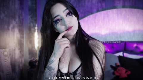 Media: Video of a pale-skinned woman with long black hair, wearing heavy makeup, in a dark, purple-lit room, with text overlay: \"All My Fears Linger in the Dark.\