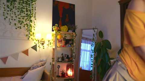 Media: Video of a cozy, colorful bedroom with a wooden bed, green ivy wall, yellow lamp, bookshelf, potted plants, and a vibrant abstract painting.