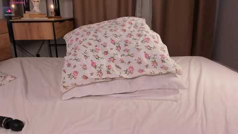 Media: A video of a neatly made bed with a white duvet and a floral-patterned pillow. The background features a wooden bedside table with a lamp, a framed picture, and a vase.