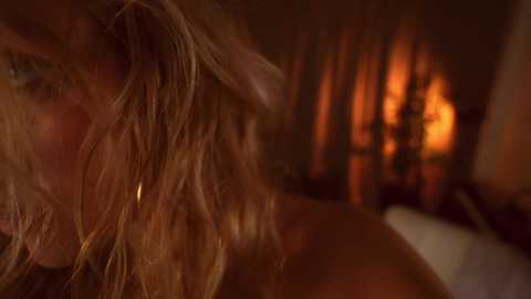 Media: A close-up video of a person with messy, tousled blonde hair, partially illuminated by a warm, orange-tinted fireplace in the background.