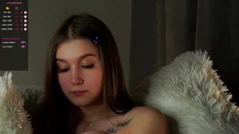 Media: Video of a young woman with long brown hair, wearing a black top, lying on a white furry blanket, looking serene.