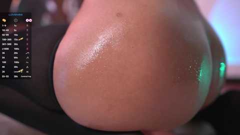 Media: Close-up video of a woman's backside, partially clothed, with a shiny, oiled surface. The background is blurred, showing a calendar and a green light.