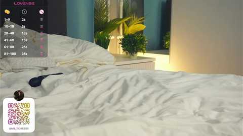 Media: Video of a messy white bed with a black bra on the sheets, green plants in the background, and a QR code on the bottom left.