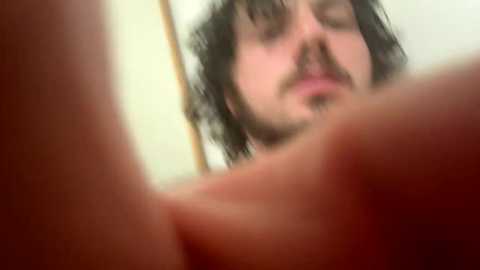 Media: Video of a bearded man with messy hair, wearing a red t-shirt, blurry in the foreground, with a close-up view of a hand.