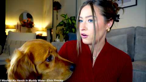 Media: Video of a young woman with fair skin and light brown hair in a bun, wearing a red top, and a golden retriever in a living room with beige furniture, a green plant, and a lamp.