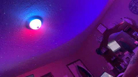 Media: Video of a bedroom ceiling with a blue and purple LED light strip, featuring a circular white light. A wooden desk with multiple computer monitors is visible in the background.