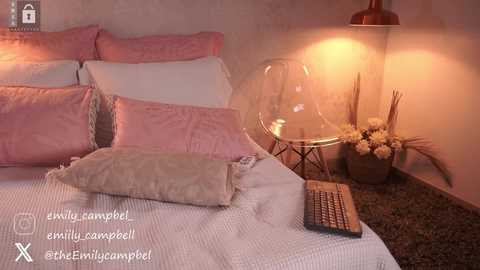 Media: Video of a cozy bedroom with a pink bed, white pillows, beige throw, clear chair, glass table, and warm lighting.