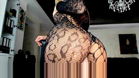 Media: Video of a woman in a black lace dress, revealing her buttocks, standing in a dimly lit living room with a chandelier, bookshelves, and a framed painting in the background.