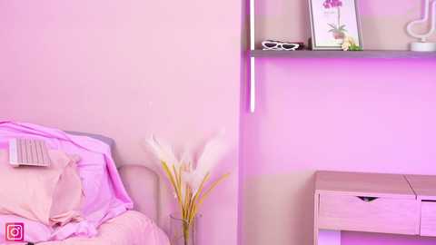 Media: Video of a minimalist, pink-themed bedroom with a white metal bed, a vase of white flowers, a small wooden desk, and a shelf with books and decorative items.