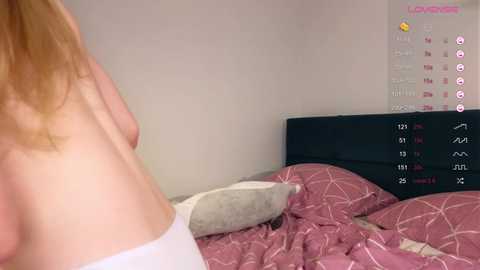 Media: Video of a woman's bare back and side, wearing a white thong, in a bedroom with a pink-patterned bedspread, a gray pillow, and a calendar on the wall.