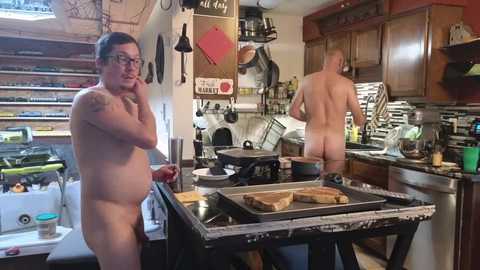 Media: Video of a messy kitchen with two nude men, one cooking, the other washing dishes, surrounded by clutter and appliances.