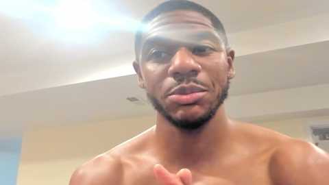 Media: Video of a shirtless, muscular Black man with a short beard, sticking out his tongue and making a \"peace\" sign. Background shows a modern, indoor setting with light-colored walls and a ceiling.