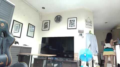 Media: Video of a bright, modern living room with a flat-screen TV, decorative frames, a blue fan, and a gaming chair.