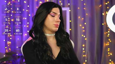 Media: Video of a light-skinned, feminine-presenting person with long, wavy black hair, wearing a black top and sparkling choker, set against a purple and gold bokeh background, with a countdown timer overlay.