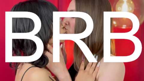 Media: Video featuring two women with medium-length straight hair, one with black hair and the other with brown hair, kissing passionately. The background is a vibrant red with a blurred, glowing lamp. Bold white text \"BBR\" overlaid.