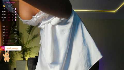 Media: A close-up video of a white, lacy bra strap being pulled down by a woman's hand, set in a dimly lit room with greenery and streaming app interface.