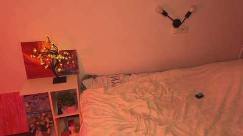 Media: A video of a bedroom with a bed covered in white sheets, a red light source illuminating a wall-mounted lamp, and colorful, abstract artwork on the nightstand.