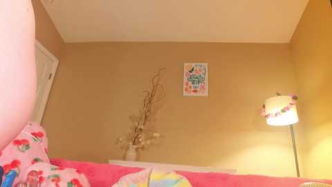 Media: Video of a cozy, yellow-walled bedroom with a bed covered in pink and colorful blankets. A white lamp casts a warm glow, and a framed \"LOVE\" sign hangs on the wall.