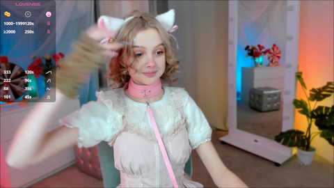 Media: A video of a young woman in a pink, lace-trimmed dress with white cat ears, sitting in a room with a mirror and colorful lighting, wearing a pink collar.