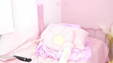 Media: A video of a messy, pink-themed bedroom with a white TV, a black remote, and a large stuffed animal on a bed covered in pastel sheets. The room has soft, pastel walls and a pink chair.