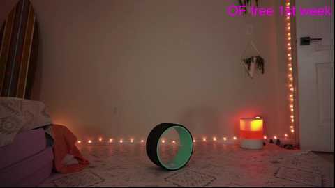 Media: Video of a cozy bedroom with a teal yoga wheel, a string of fairy lights, a white lamp, a bed, and a plant, set against a cream wall.