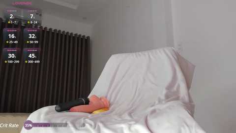 Media: Video of a beige sofa covered in white sheets, with a black remote control and orange pillow on the cushion. A white radiator and dark curtains in the background.