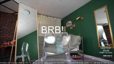 Media: Video of a modern bedroom with green walls, a brick wall, a bed with white sheets, and a clear acrylic chair, featuring a live stream overlay of \"BRB\" and \"0:04:44\" text.